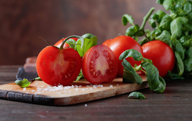 Red tomatoes with green basil on wooden table.