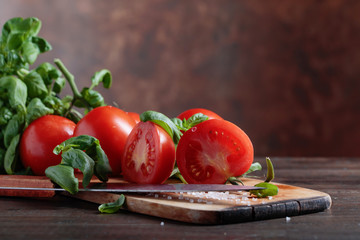Red tomatoes with green basil on wooden table.