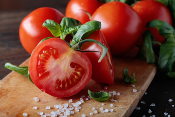 Red tomatoes with green basil on wooden table.