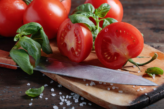Red tomatoes with green basil on wooden table.