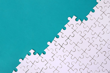 Fragment of a folded white jigsaw puzzle on the background of a blue plastic surface. Texture photo...