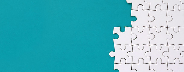 Fragment of a folded white jigsaw puzzle on the background of a blue plastic surface. Texture photo with copy space for text