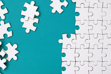 Fragment of a folded white jigsaw puzzle and a pile of uncombed puzzle elements against the...