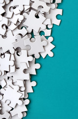 A pile of uncombed elements of a white jigsaw puzzle lies on the background of a blue surface....
