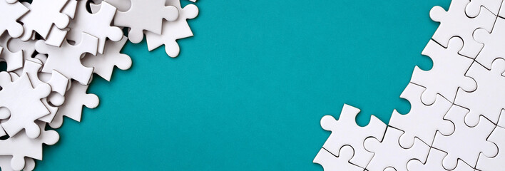 Fragment of a folded white jigsaw puzzle and a pile of uncombed puzzle elements against the background of a blue surface. Texture photo with space for text - obrazy, fototapety, plakaty