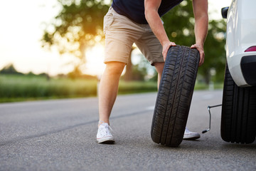 The man changes the tire to a broken car on the road