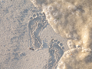 Fußspuren im Sand werden von einer Welle weggespült