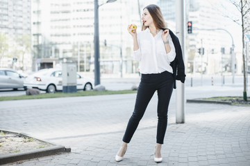 Girl in a business suit on the streets of the city with an apple. A young woman speaks through a mobile phone. The lady smiles.