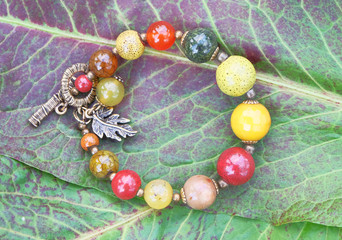 Bracelet made of ceramic beads and natural stones placed on a large leaf of the plant. Composition with women's jewelry handmade.