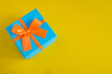 Blue gift box with orange  ribbon on the  yellow background.Top view.