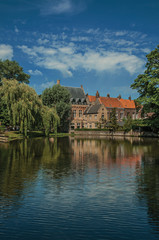 Fototapeta na wymiar Amazing lake surrounded by greenery and old brick building on the other side in Bruges. With many canals and old buildings, this graceful town is a World Heritage Site of Unesco. Northwestern Belgium.