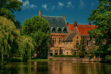 Fototapeta na wymiar Amazing lake surrounded by greenery and old brick building in Bruges. With many canals and old buildings, this graceful town is a World Heritage Site of Unesco. Northwestern Belgium. Retouched photo.