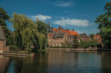 Naklejka na ściany i meble Amazing lake surrounded by greenery and old brick building on the other side in Bruges. With many canals and old buildings, this graceful town is a World Heritage Site of Unesco. Northwestern Belgium.