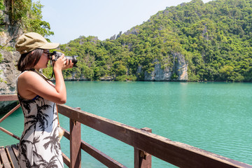 Woman tourist at Thale Nai on Koh Mae Ko island viewpoint use camera taking photos at beautiful nature landscape of Blue Lagoon (Emerald Lake) in Mu Ko Ang Thong National Park, Surat Thani, Thailand