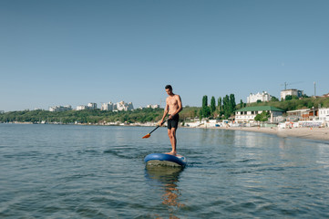guy stand up paddle boarding on quiet sea at sunset