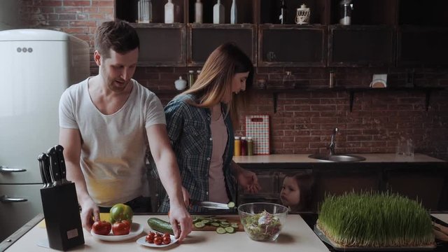 Happy Family Kitchen routine. Husband halps his wife with cooking, daughtr is around.