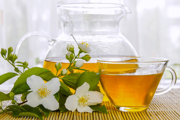 Jasmine green tea in a glass teapot and fresh jasmine flowers on a bamboo mat. Close-up.