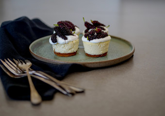 homemade personal cheesecakes with mulberries and cream topping, on top of a ceramic plate