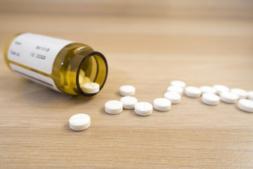 Tablets scattered from a jar on a light wooden table close up