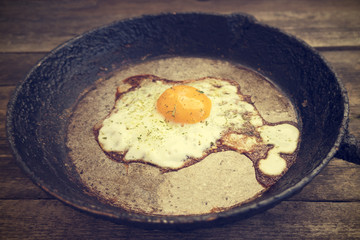One fried egg in a frying pan on a wooden background in rustic style close-up