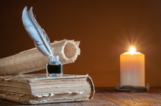 Quill pen by candle light with old paper and books