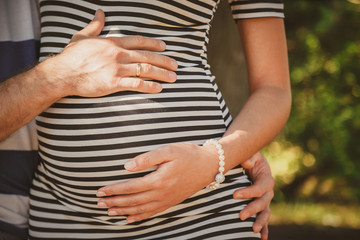 Close up portrait of happy pregnant woman together with husband hugging in summer park