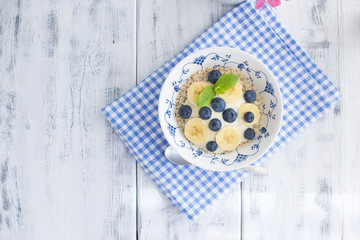 Delicious and healthy breakfast. Oatmeal with berries and banana. White wooden background and blue napkin. Good morning. View from above. Copy space