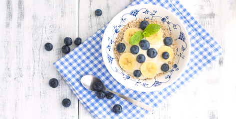 Delicious and healthy breakfast. Oatmeal with berries and banana. White wooden background and blue napkin. Good morning. View from above. Copy space