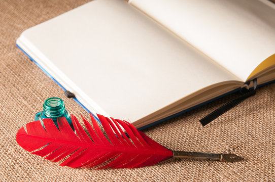 Red quill pen, a green inkwell and an open notebook on a piece of jute