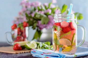 Homemade refreshing drink from pieces of strawberries, lime and mint in mason jar is on a wooden table and ready to drink