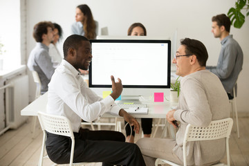 Fototapeta premium Friendly diverse colleagues having good relations and pleasant conversation at work, smiling african and caucasian coworkers talking in office, multiracial team members discussing new project idea