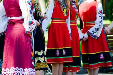 Unrecognizable girls in traditional Bulgarian costumes with red dresses and patterns on white...