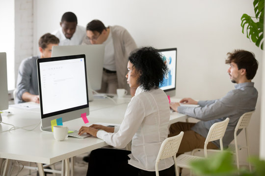 African american woman manager focused on computer work in multi-ethnic corporate office, serious black employee sending email online on desktop in coworking, diverse business people working together