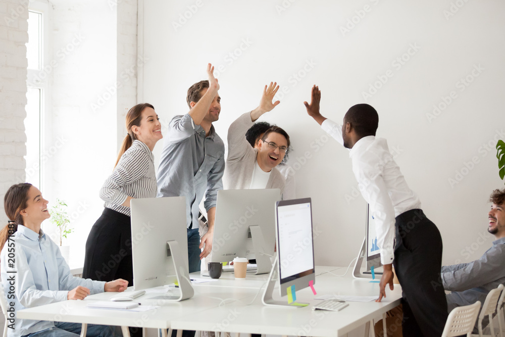 Poster Happy multi-ethnic employees sales team giving high five together celebrating corporate success and good relations, diverse group of office people joining hands excited by common victory achievement