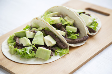 Three mexican tacos on the bamboo board on a white wooden background, side view. Closeup.