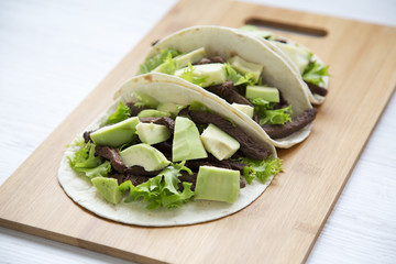 Corn tortillas with grilled beef, avocado and lettuce on wooden board, closeup. Side view.