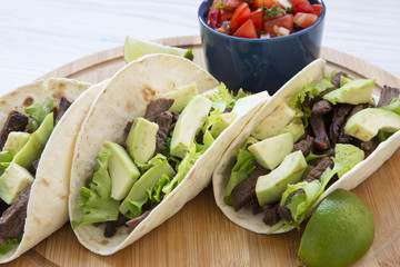 Mexican food. Tacos with salsa on the bamboo board on a white wooden background, side view.