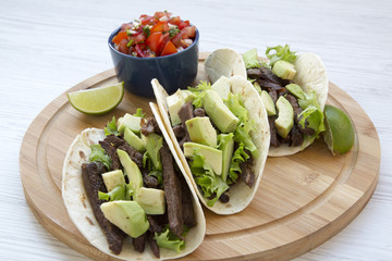 Mexican tacos with salsa on the bamboo board on a white wooden background, side view. Fajitas taco tortillas. Closeup.
