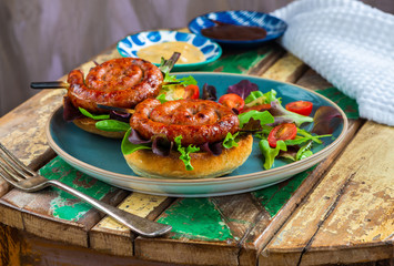Chilli pork pinwheel sausages on a bun with fresh green leaf lettuce salad