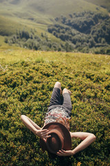 traveler hipster girl in hat lying on grass in sunny mountains and relaxing. summer vacation. space...