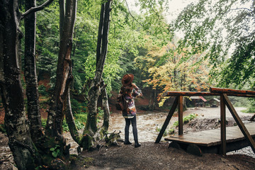 Fototapeta na wymiar stylish hipster girl in hat with backpack walking in forest in mountains. traveler woman exploring woods. travel and wanderlust concept. atmospheric moment, space for text