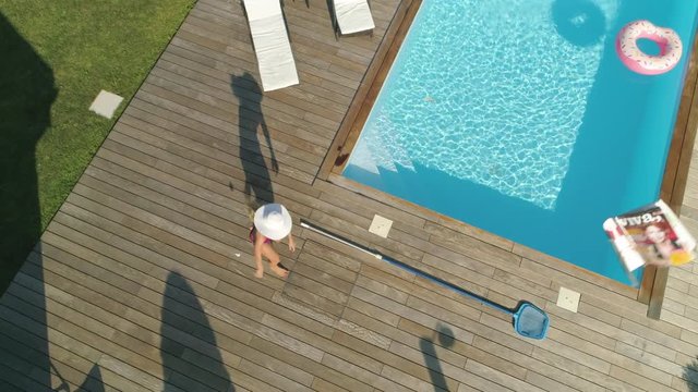 SLOW MOTION, POV, AERIAL: Blonde woman chasing around drone invading her privacy while she sunbathes in her garden. Funny angry girl next door throwing things at remote controlled plane stalking her.