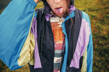 happy traveler hipster girl in colorful raincoat, showing colorful blue tongue from eating blueberries in sunny mountains. summer vacation. space for text. happy moment