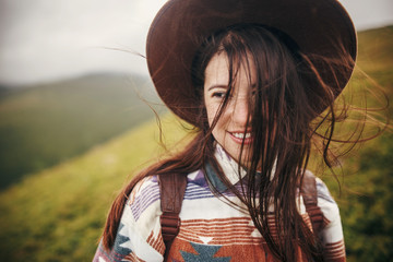 happy traveler hipster girl in hat with windy hair, relaxing in sunny mountains. space for text....