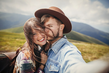 happy hipster couple making selfie on top of sunny windy mountains.  family hugging and smiling. summer vacation. space for text. atmospheric moment. travel and wanderlust concept