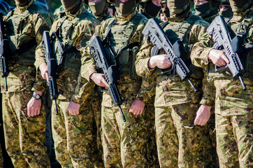 Unrecognizable soldiers in military uniform and in masks standing in a row with guns in their hands...