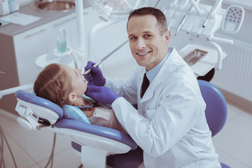 Obraz premium Working in dentistry. Vigorous experienced male dentist using dental instrument while staring at camera