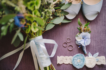 Bridal morning details composition. Top view of bride's garter, bouquet of field flowers with ribbons, boutonniere and leather shoes. Flat lay.