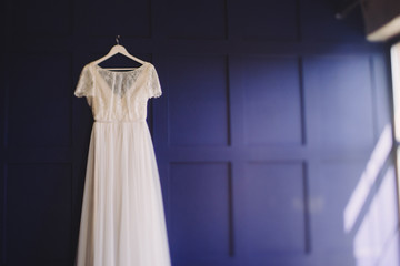 Wedding fashion. Bridal morning details. White lace dress hanging on blue wall.