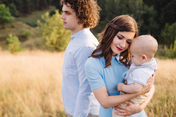 Fototapeta premium Young happy caucasian couple with little baby boy. Parents and son walking and having fun together. Mother and father playing with toddler outdoors. Family, parenthood, childhood, happiness concept.